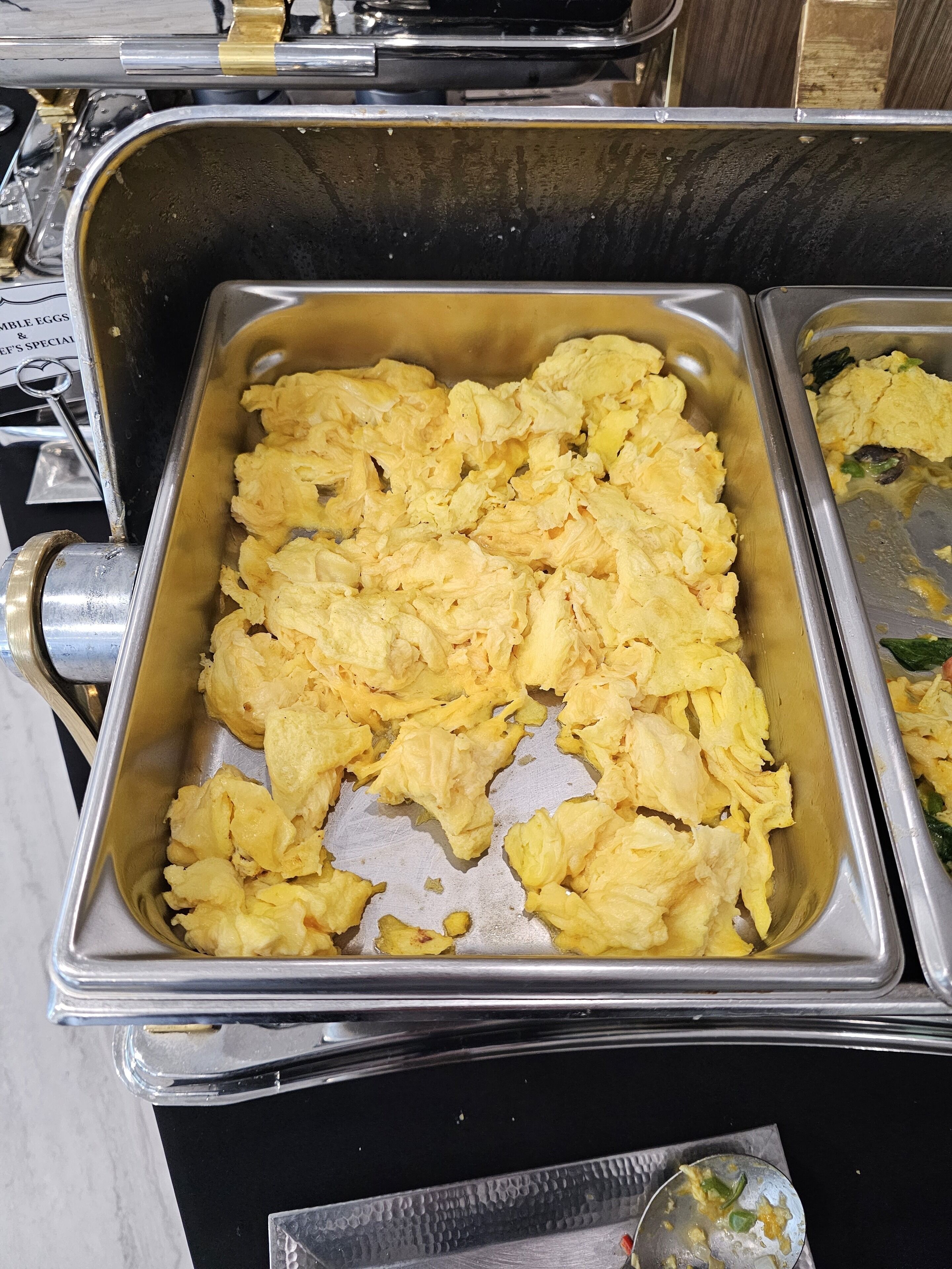 A buffet with scrambled eggs in a metal serving tray.