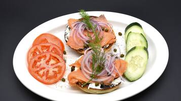 A plate with bagels topped with smoked salmon, red onion, capers, and dill, accompanied by slices of tomato and cucumber.