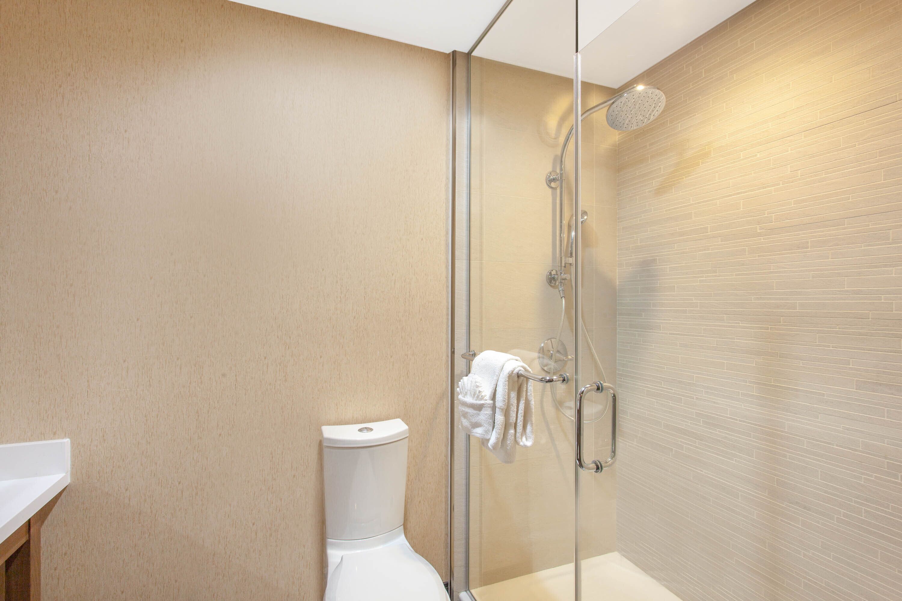A modern bathroom with a glass-enclosed shower, a white toilet, and a beige tiled wall.