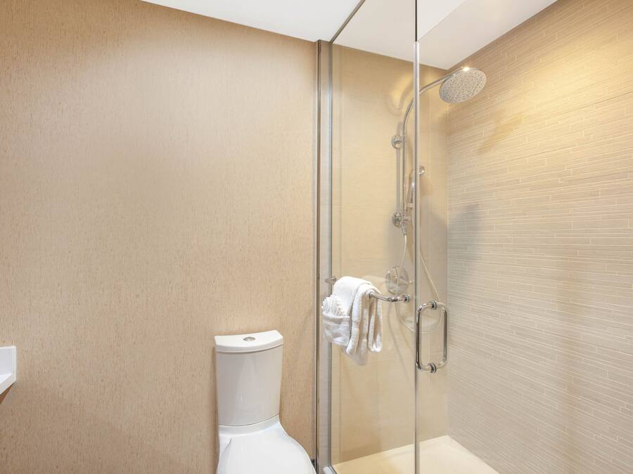 A modern bathroom with a glass-enclosed shower, a white toilet, and a beige tiled wall.