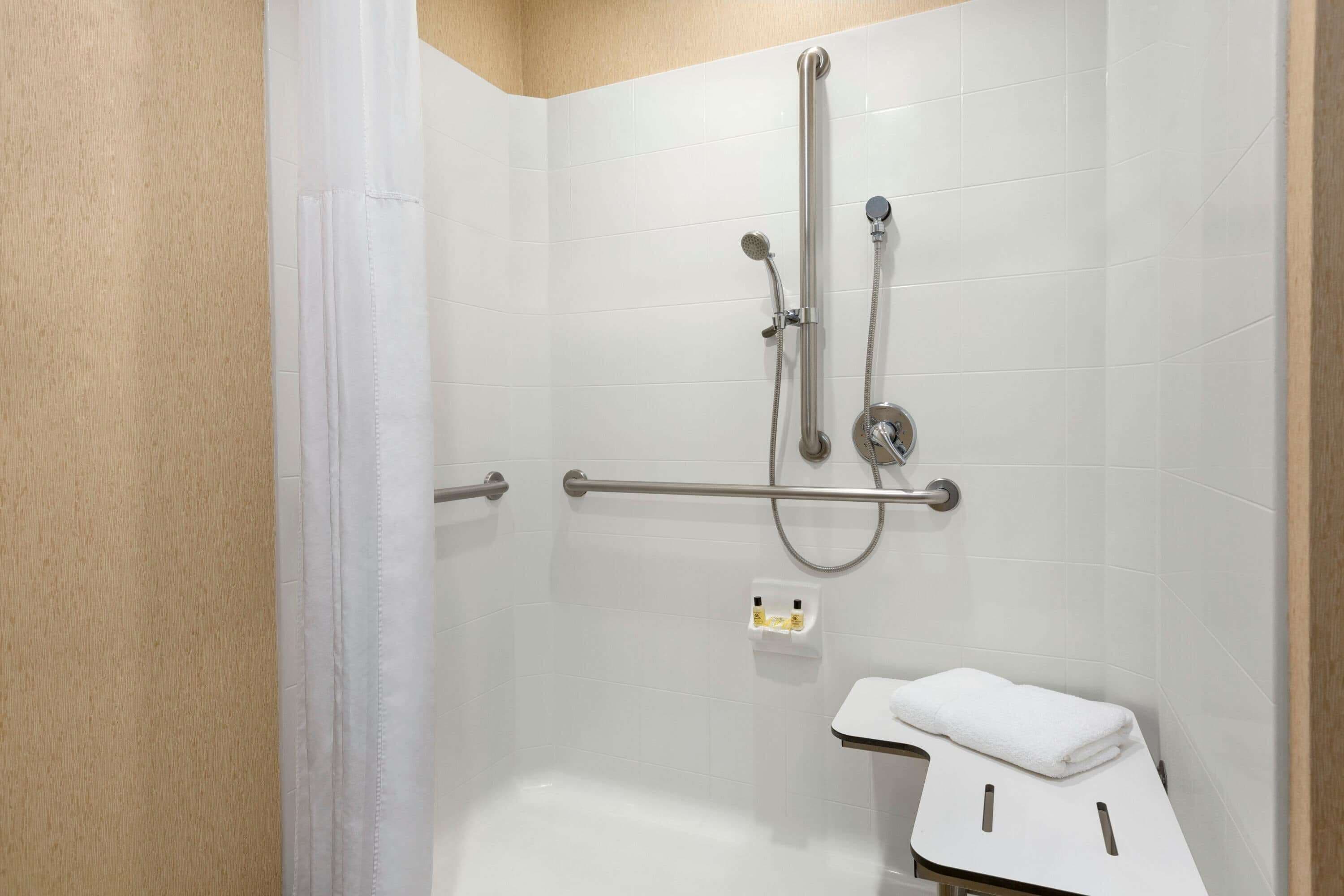 A shower area with a grab bar, a handheld showerhead, and a towel rack.