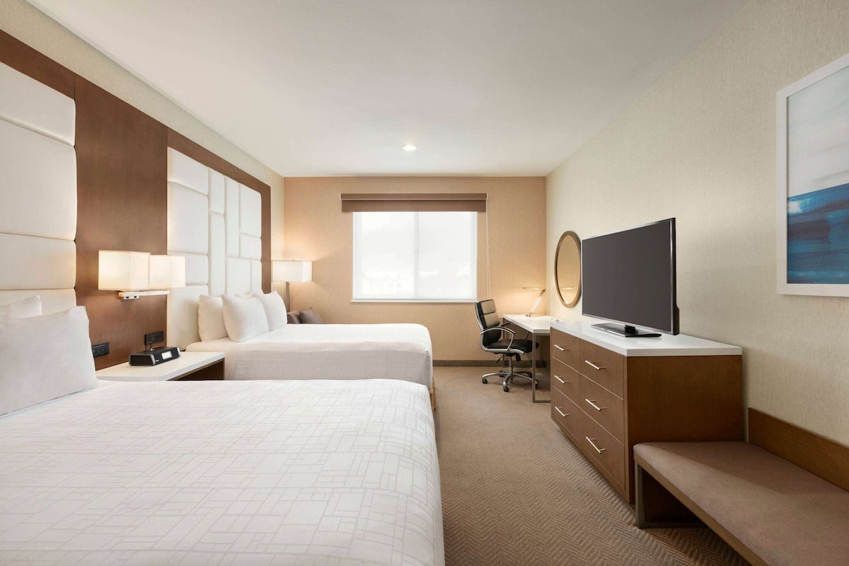 A hotel room with two beds, a desk, a television, and a window.