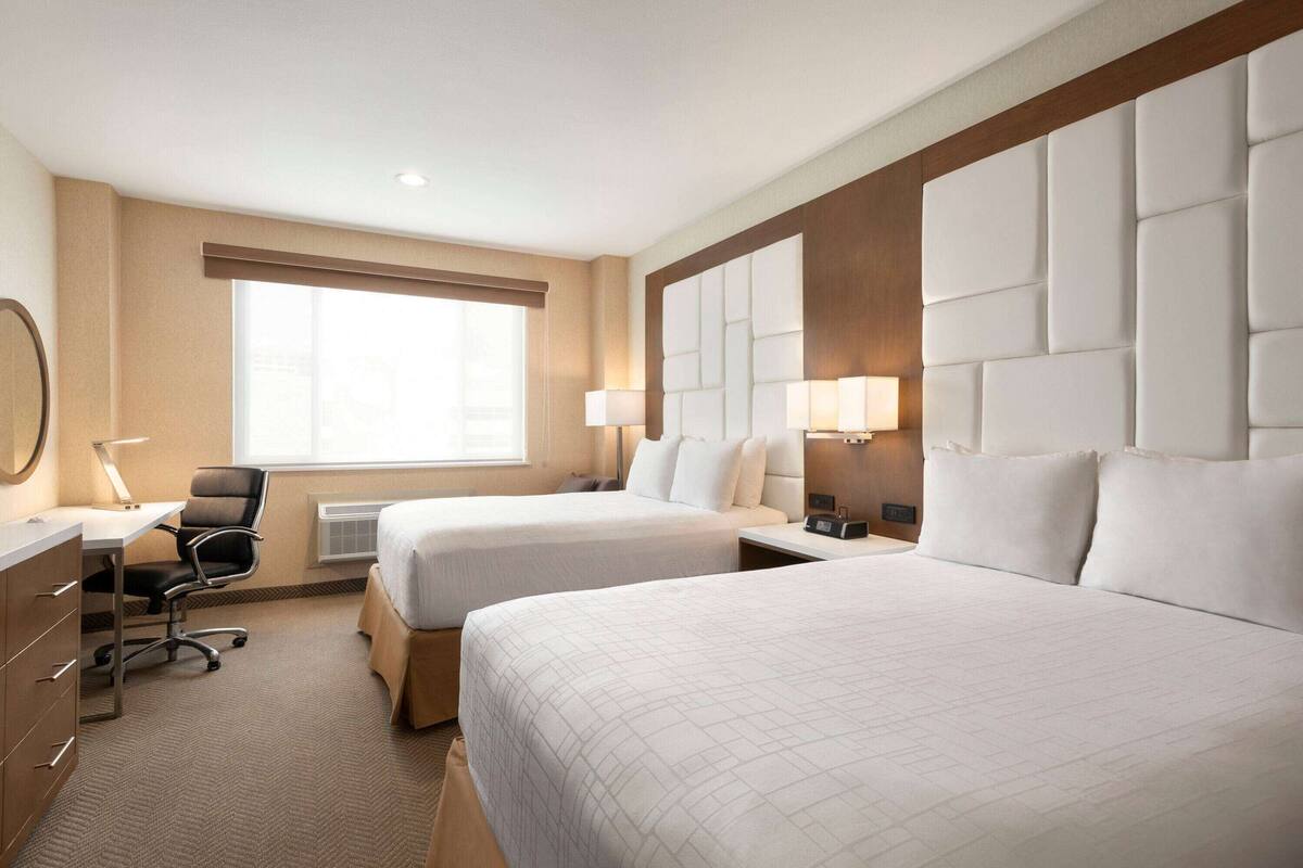 A hotel room with two beds, a desk, a chair, and a large window.