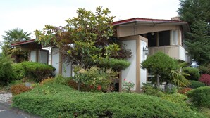 A two-story house with a balcony, surrounded by well-maintained gardens and various plants.