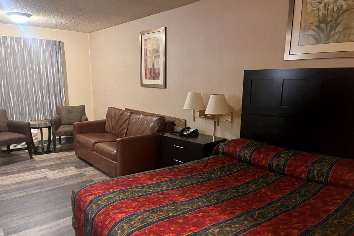 Ein Hotelzimmer mit einem Bett, einer Couch, einem Schreibtisch mit Telefon, zwei Wandlampen und einem Gemälde an der Wand.