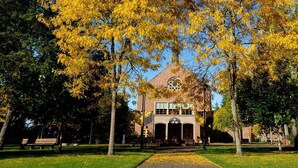 A building with a central tower and arched windows, surrounded by trees with yellow leaves.