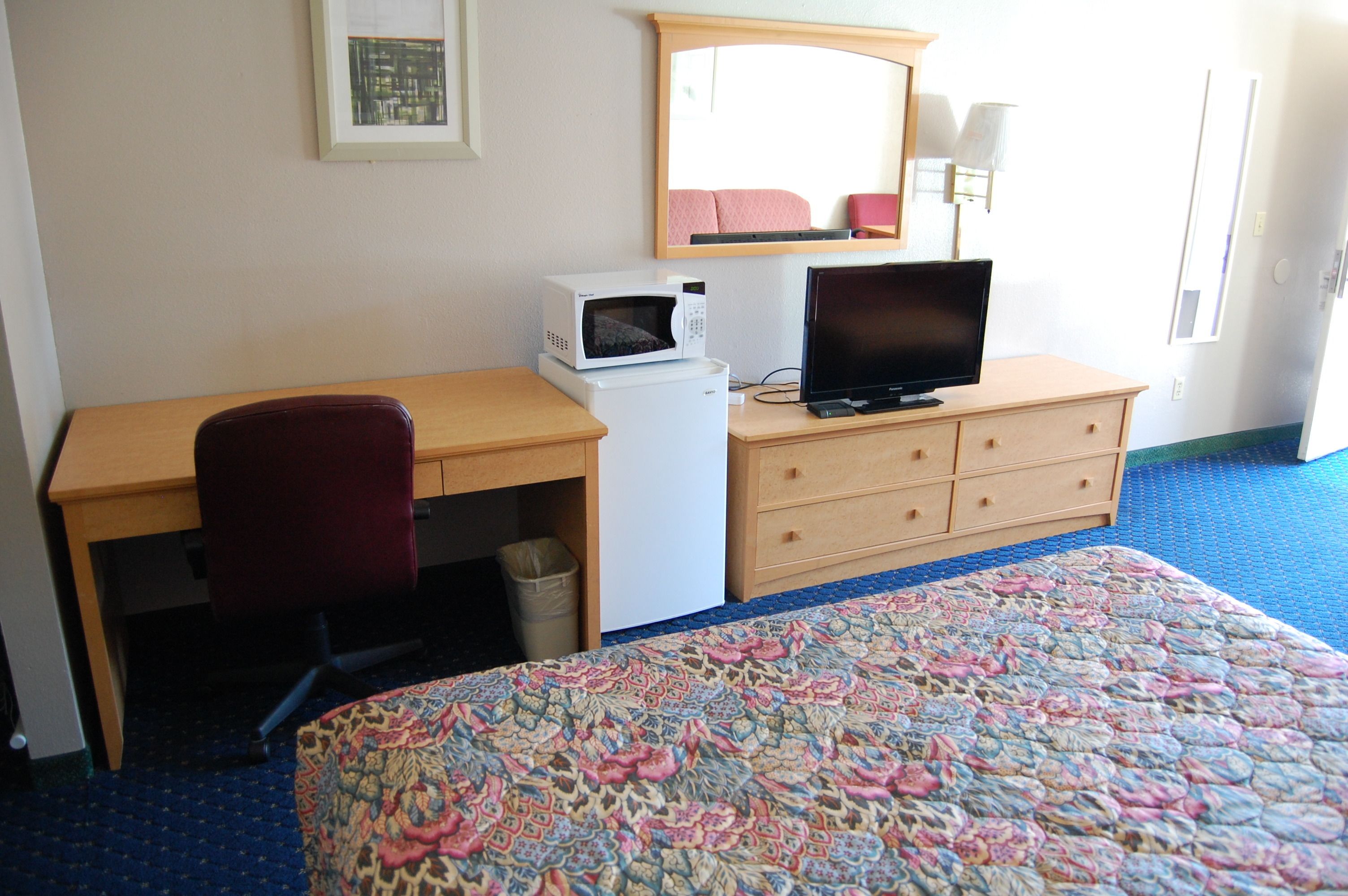 A hotel room with a bed, a desk with a computer, a microwave, and a chair.