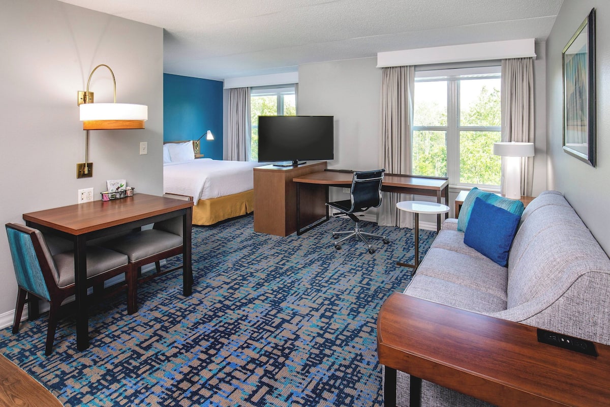 A hotel room with a bed, desk, TV, sofa, and a patterned carpet.