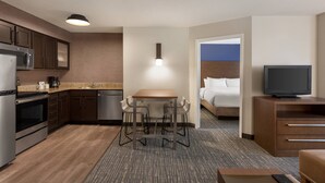 Ein kompaktes Hotelzimmer mit einer Küchenzeile, einem Essbereich mit Barhocker, einem Bett und einem Fernseher.