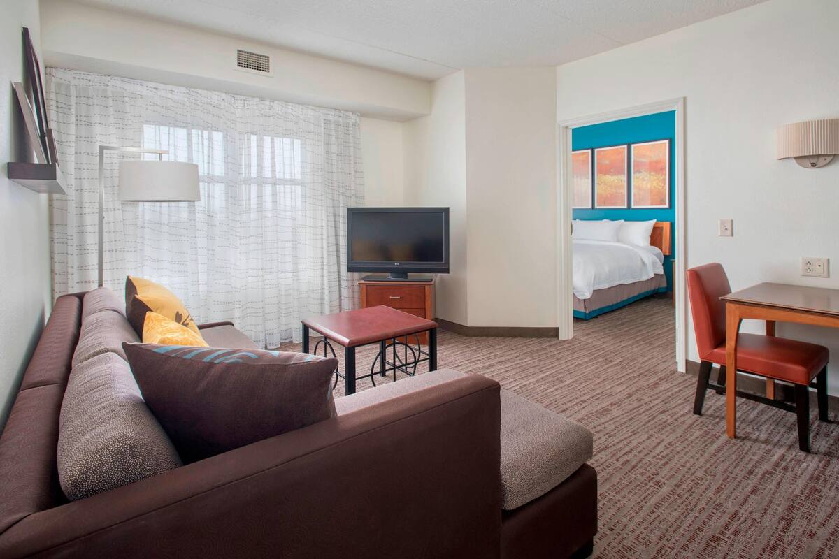 A hotel room with a sofa, a TV, a small table, a bed, and a chair.
