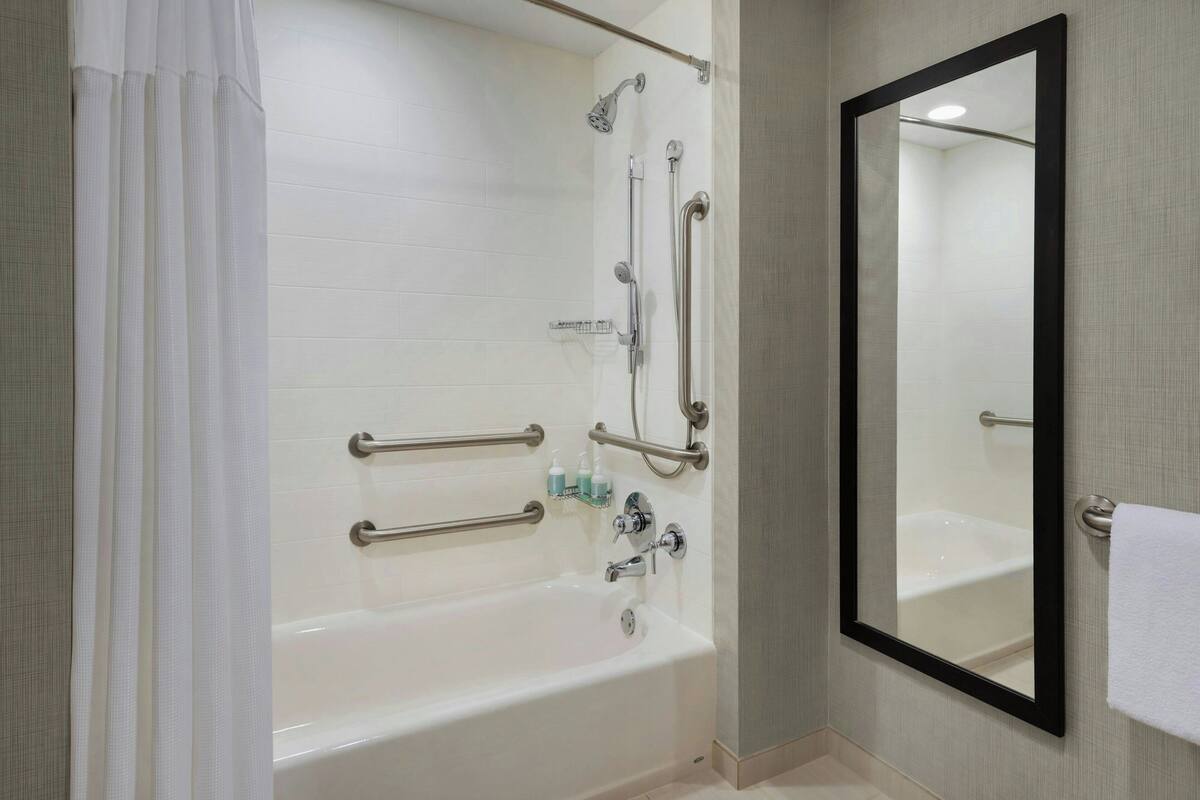 A modern bathroom with a white bathtub, a large mirror, and grab bars for accessibility.