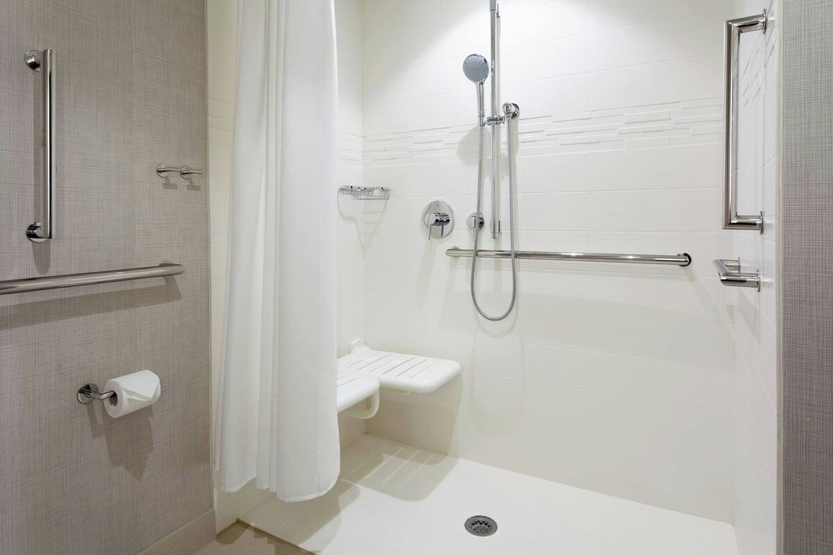 A modern bathroom with a walk-in shower, grab bars, a toilet paper holder, and a shower control panel.
