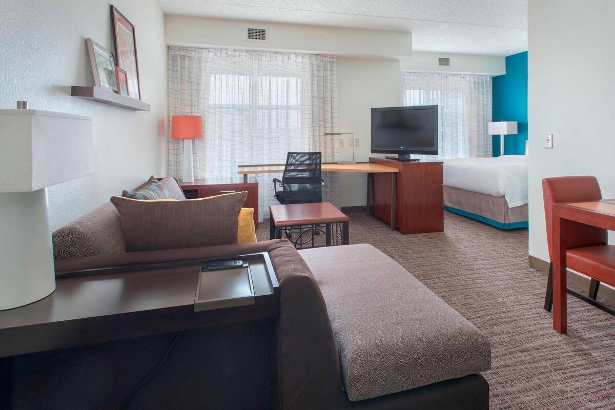 A hotel room with a sofa, a desk with a computer, a TV, a bed, and a small table.