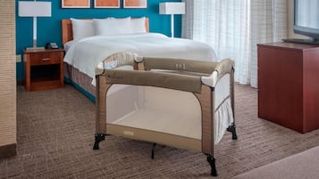 A hotel room with a bed, a TV, a bedside table with a lamp, and a crib.