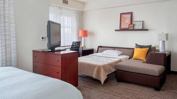 A hotel room with a bed, a desk with a computer, a chair, a sofa, and a TV.