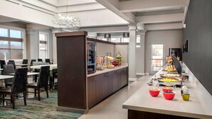 Un comedor moderno de hotel con un bufé, que incluye diversos alimentos y una zona de estar con mesas y sillas.