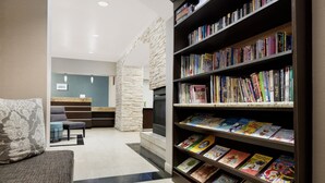 A reception area with a stone wall, a reception desk, a seating area with a couch and chairs, and a bookshelf filled with books. - Residence Inn by Marriott Saddle River (Saddle River)