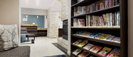 Un área de recepción con pared de piedra, mostrador de recepción, zona de estar con sofá y sillones, y una estantería llena de libros.