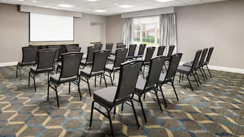 A conference room with a large screen, rows of chairs, and a carpeted floor.