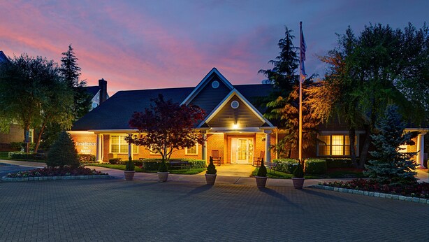 A brick building with a triangular roof, a flagpole, and a well-lit entrance. - Residence Inn by Marriott Saddle River (Saddle River)