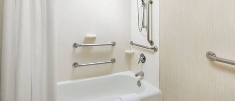 Un baño estándar con bañera, barras de apoyo, cabezal de ducha y toallero.