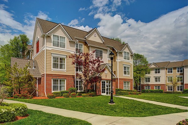 A multi-story residential building with a brick facade, multiple windows, and a well-maintained lawn.