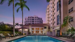 Un hôtel doté d’une piscine, de palmiers et d’un bâtiment à plusieurs étages avec des balcons.