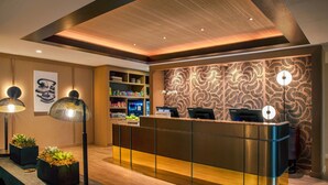 Un hall d’accueil d’hôtel moderne, avec un plafond en bois, un mur décoré de motifs et un comptoir d’accueil équipé d’un ordinateur.