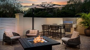 Une terrasse extérieure dotée d’un foyer, de meubles en osier et d’un espace barbecue.