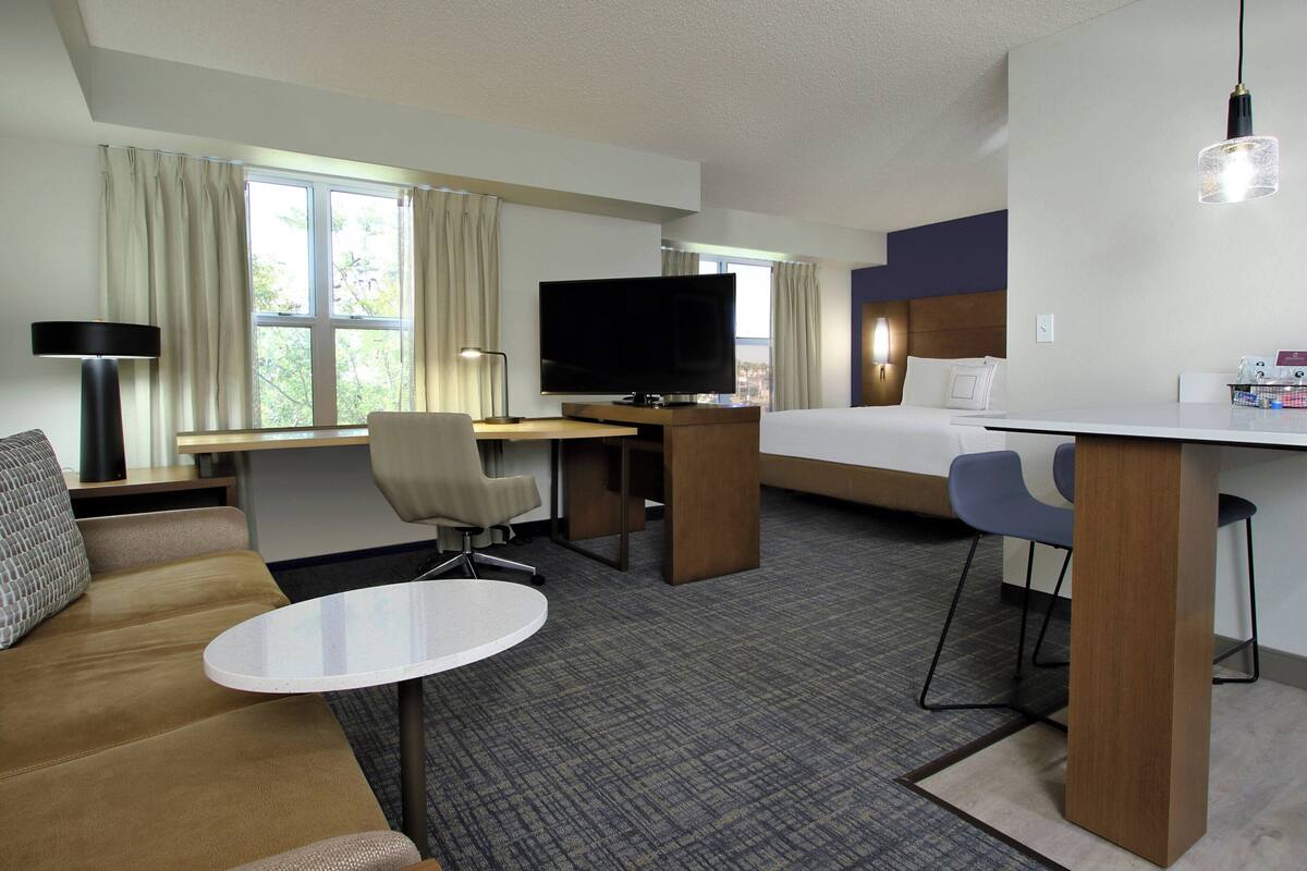 A hotel room with a bed, a desk, a television, a sofa, and a small table.