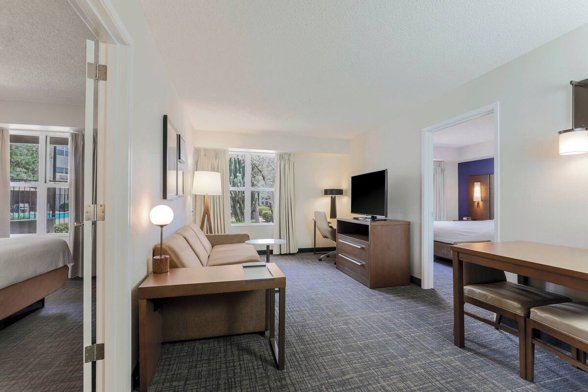 A hotel room with a bed, a sofa, a desk, a TV, and a window with curtains.