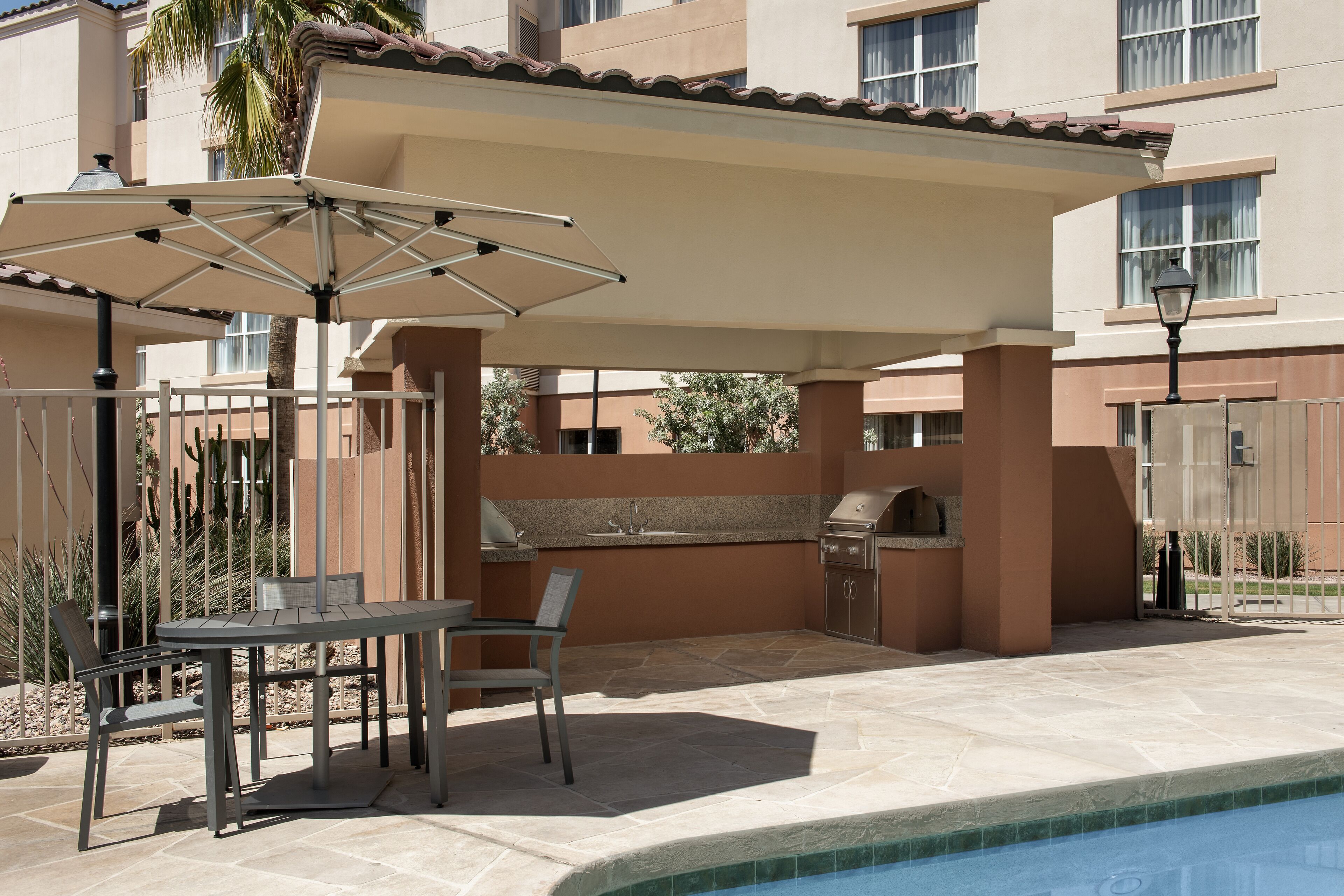 An outdoor patio with a table and chairs, a grill, and a pool.