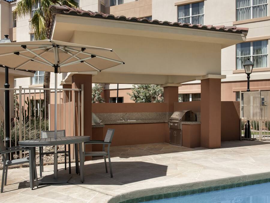 An outdoor patio with a table and chairs, a grill, and a pool.