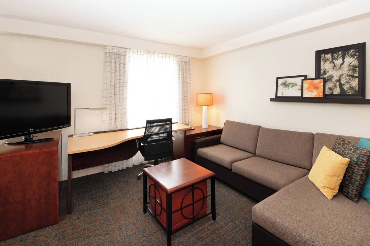 Habitación de hotel con televisión de pantalla plana, escritorio, silla, sofá y una pequeña mesa.