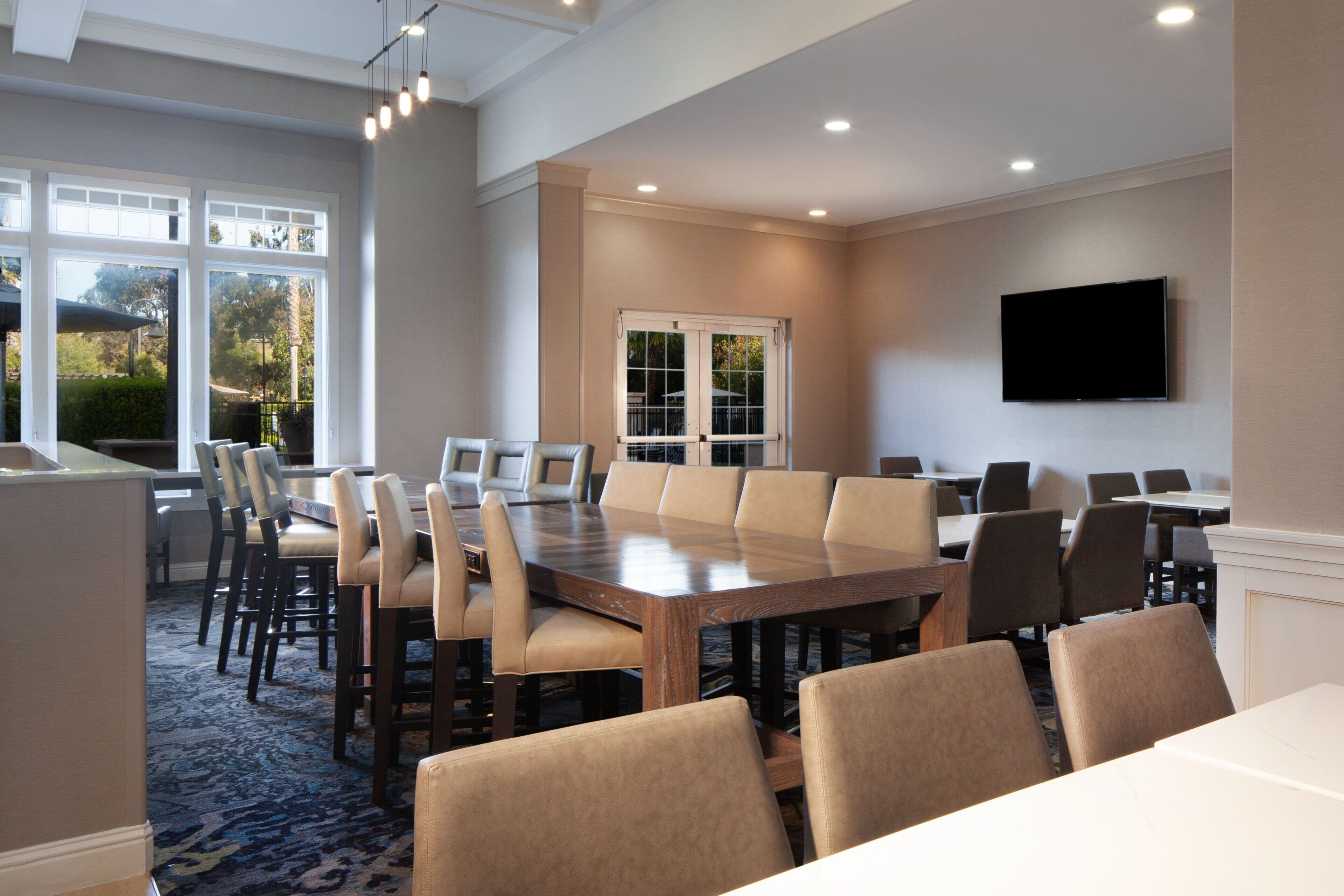 A conference room with a large wooden table, beige chairs, and a flat-screen TV mounted on the wall.