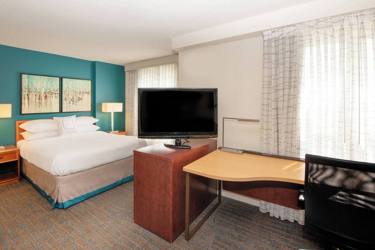 Una habitación de hotel con cama, escritorio, televisión y obras de arte en la pared.
