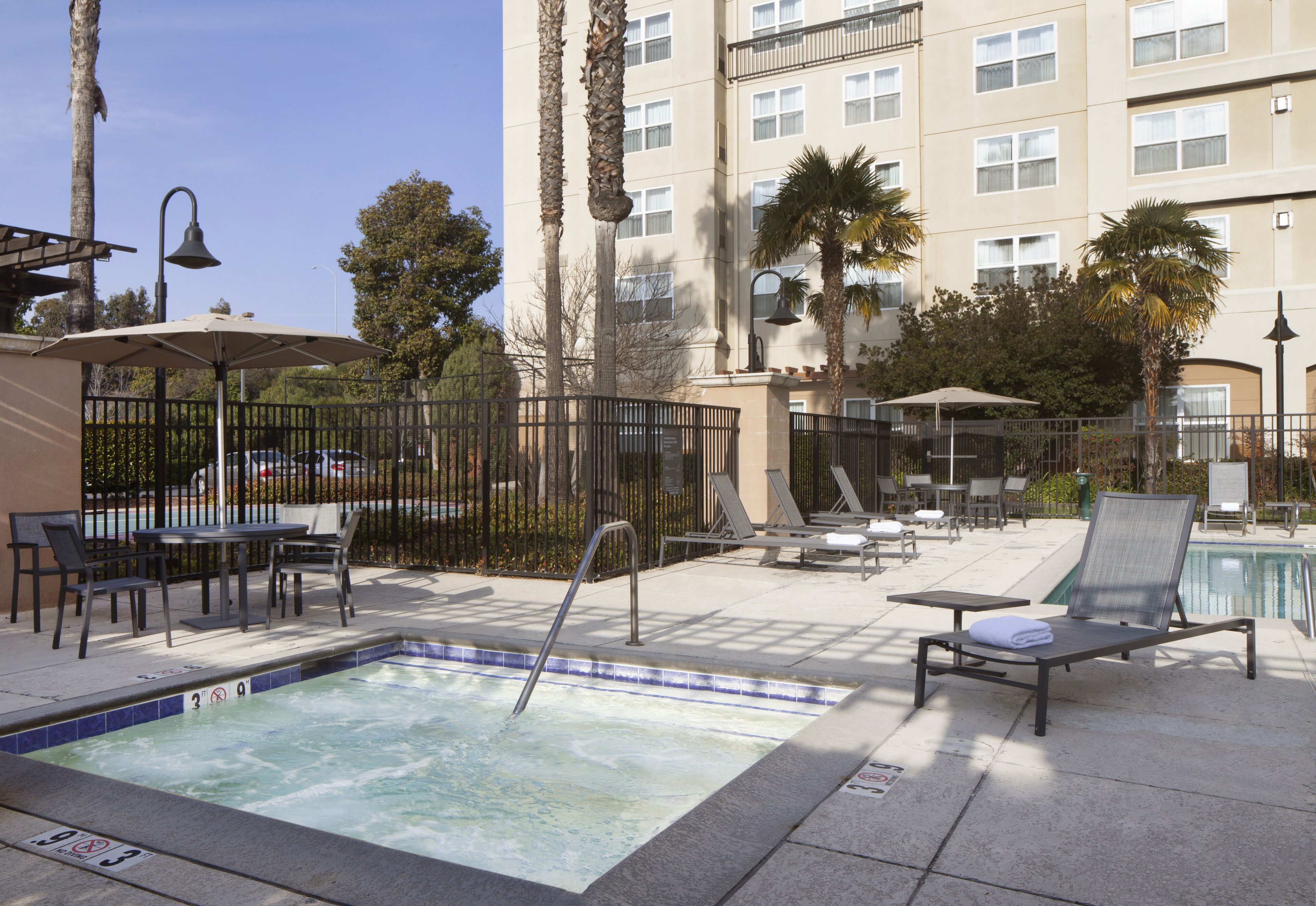 A hotel pool area with a hot tub, lounge chairs, and umbrellas.