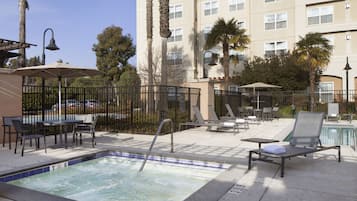 A hotel pool area with a hot tub, lounge chairs, and umbrellas.