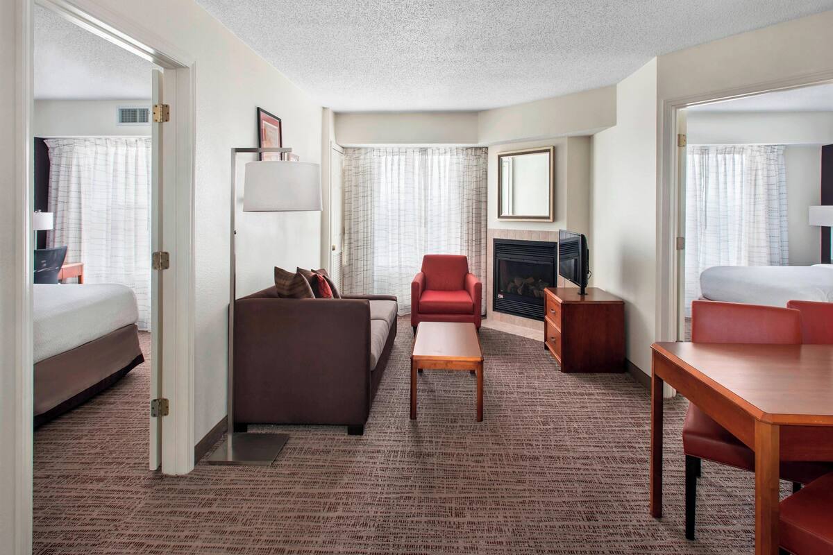 Una habitación de hotel con una cama, un sofá, un sillón rojo, una mesa de centro de madera y un televisor.