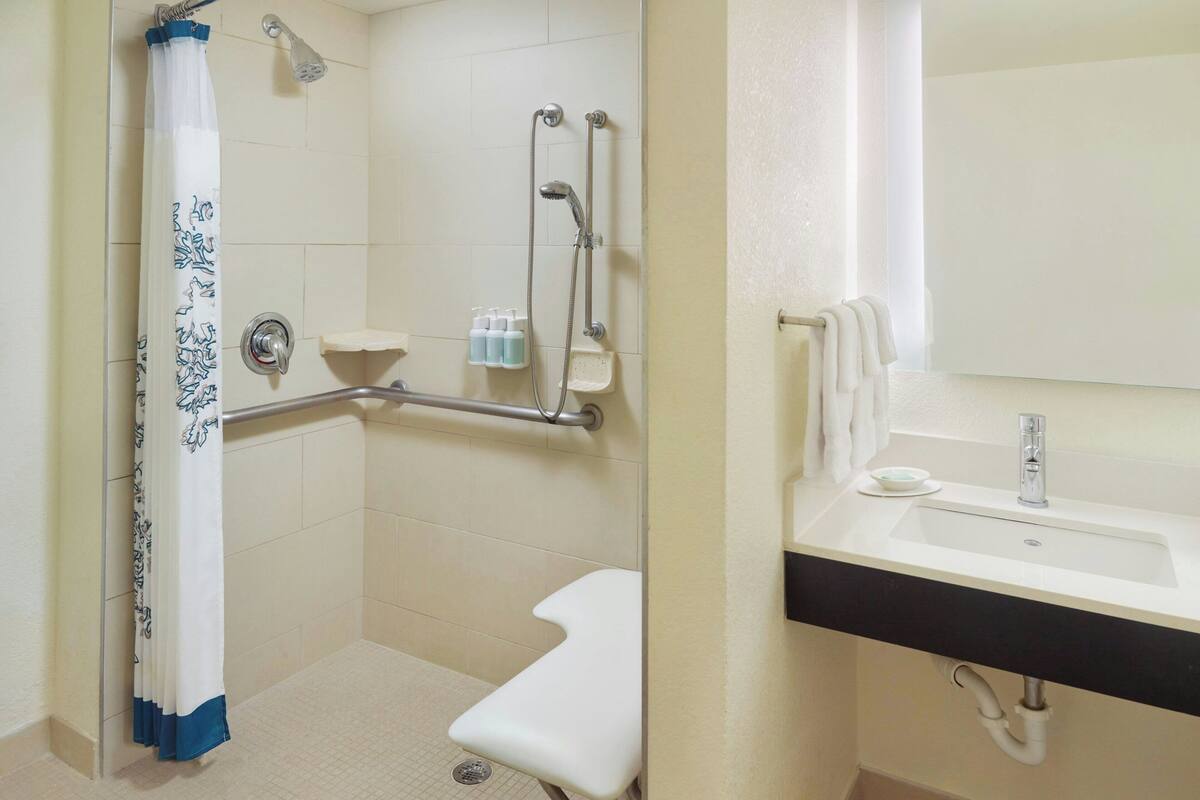 Ein Badezimmer mit Dusche, Haltegriffen, Waschbecken und Toilette.