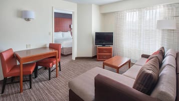 Quarto de hotel com área de refeições, sofá, televisão e cama.