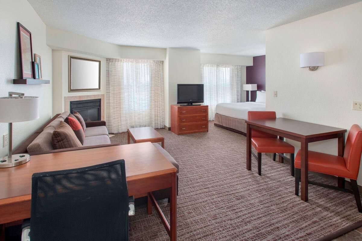Ein Hotelzimmer mit einer Couch, einem Esstisch, einem Fernseher, einem Bett und einem Schreibtisch.