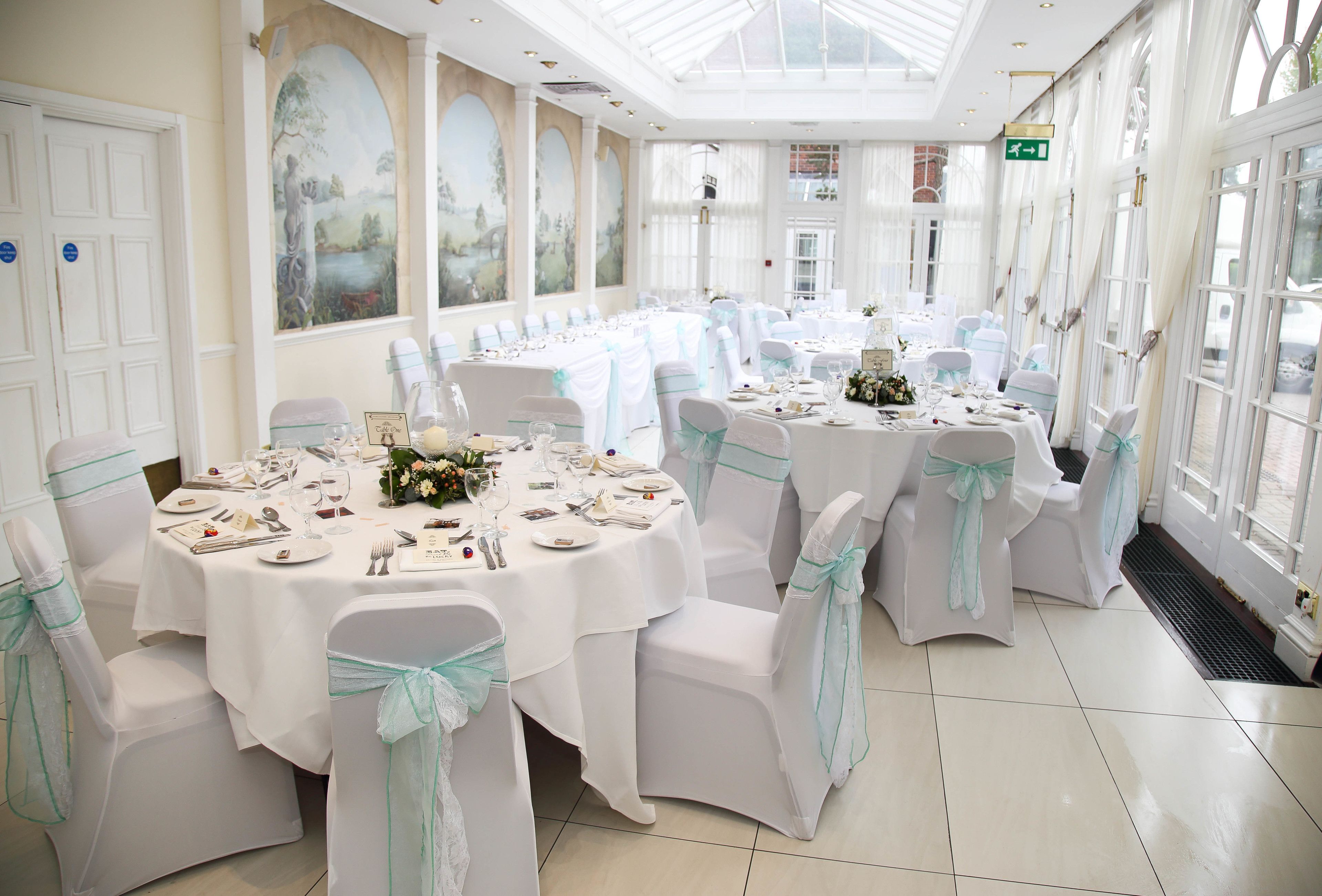 Un salón de banquetes con mesas redondas, manteles blancos y sillas con cintas azul claro.