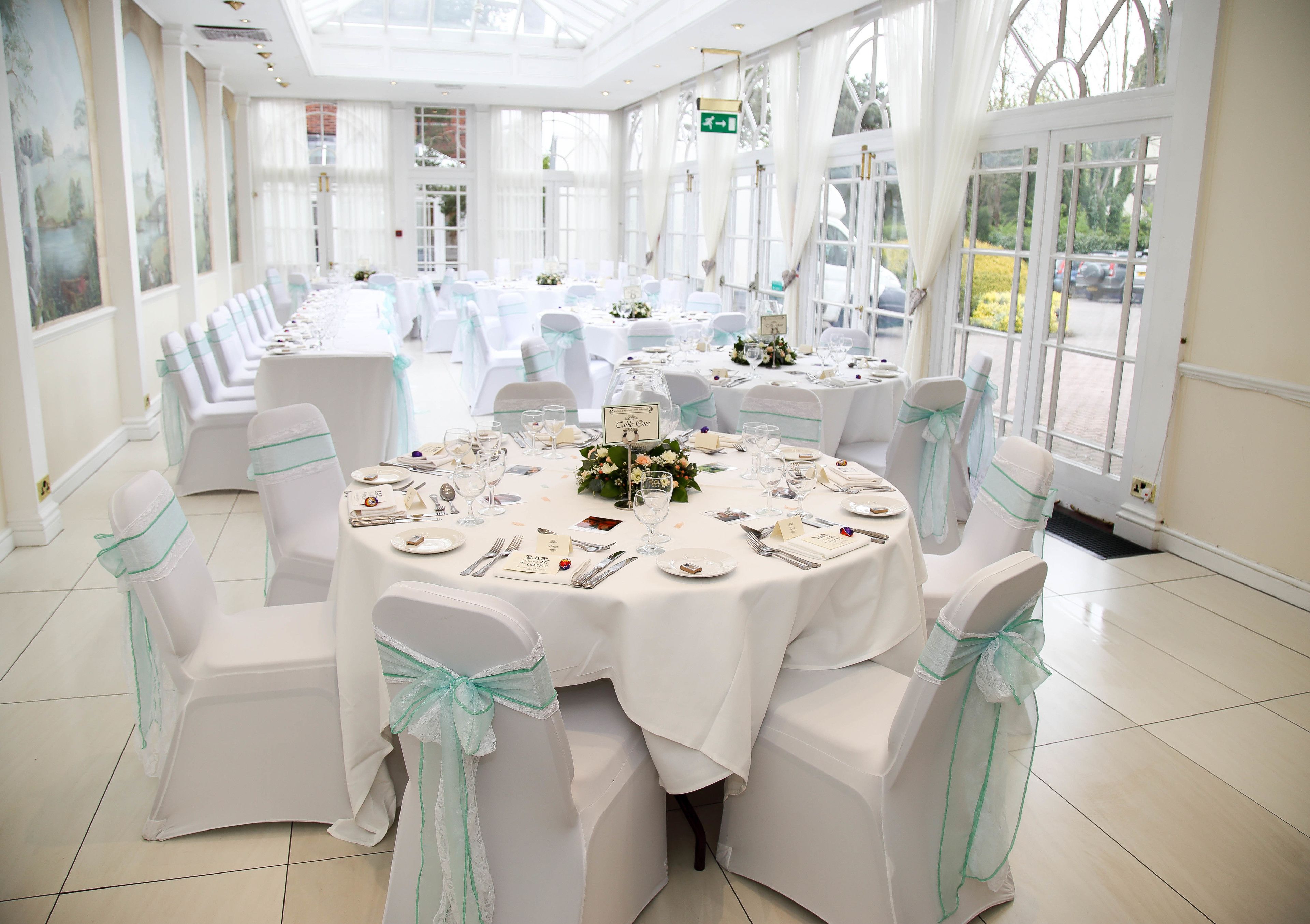 A banquet hall with round tables set for a formal event, featuring white tablecloths and chairs with green sashes.
