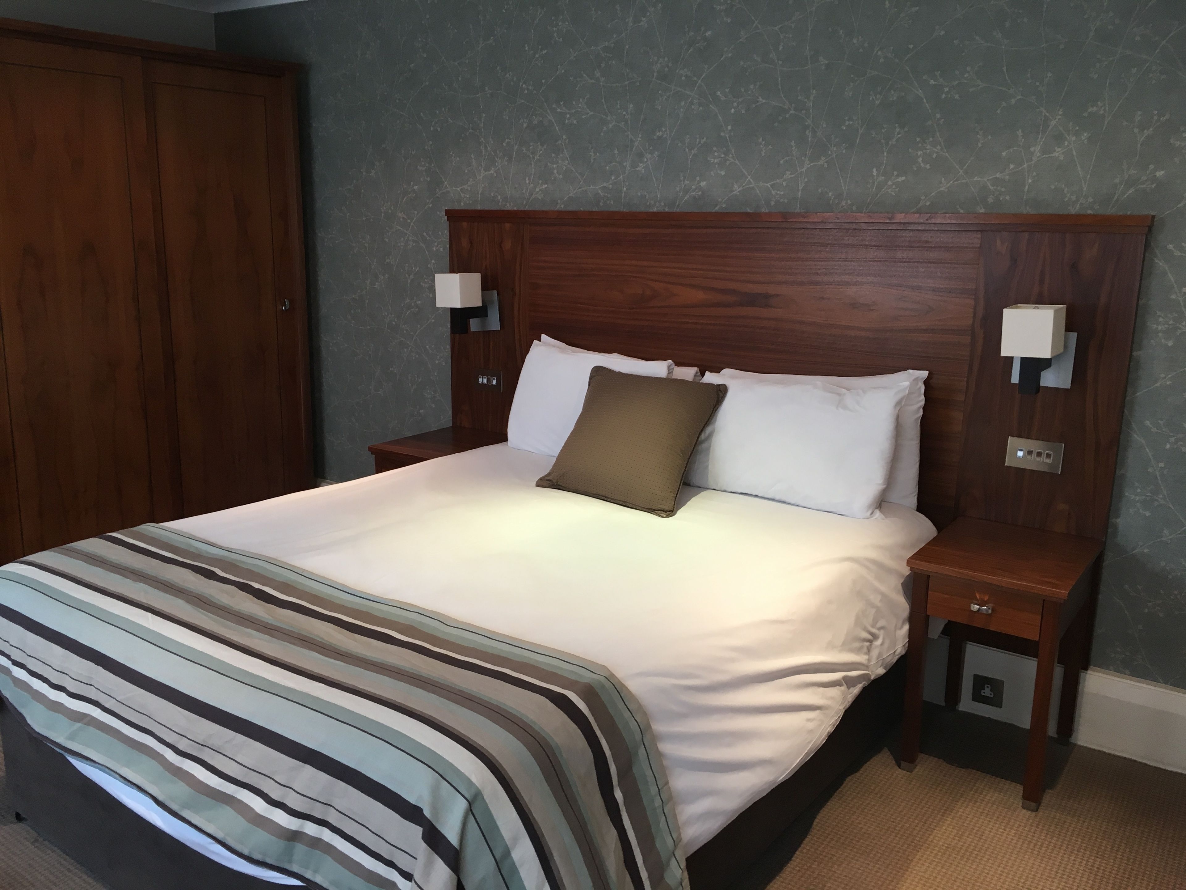 A neatly made bed with a striped blanket, a wooden headboard, two bedside tables with lamps, and a wardrobe.