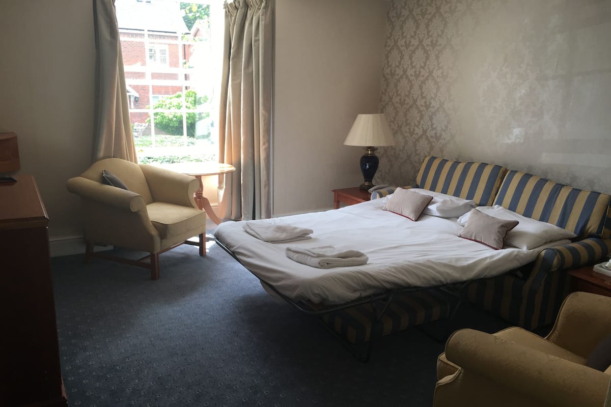A hotel room with a bed, two chairs, a lamp, and a view of the outside.