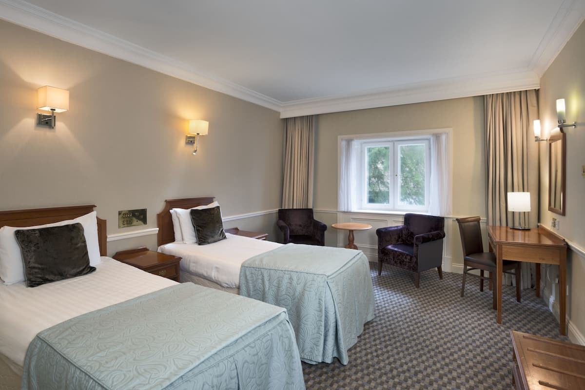 A hotel room with two beds, a desk, a chair, and a window with curtains.