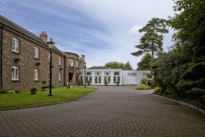A paved courtyard with stone buildings, a white structure with large windows, and surrounding greenery. - Quorn Country Hotel (Loughborough)