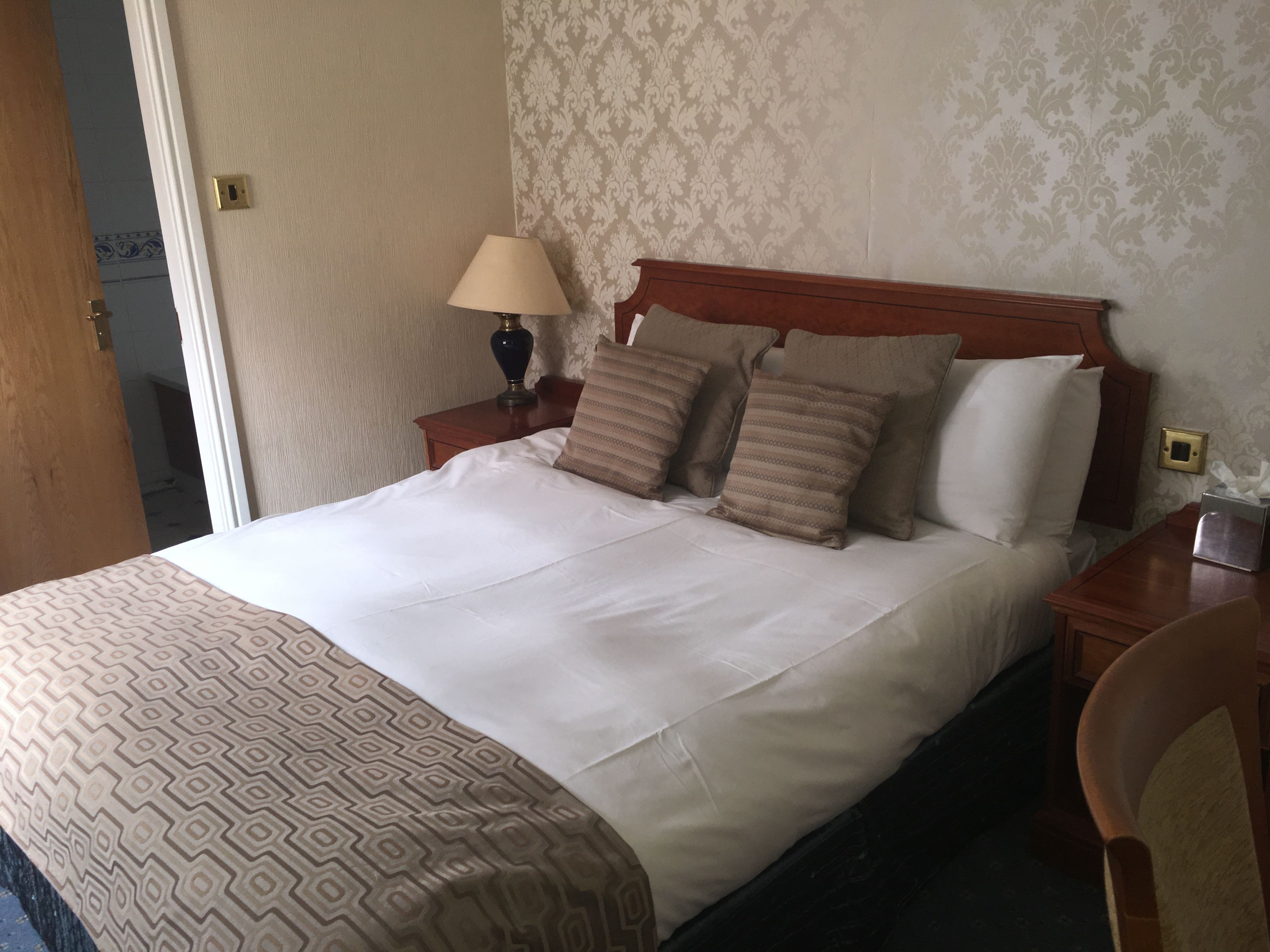 A neatly made bed with a patterned bedspread, a wooden headboard, and several pillows.