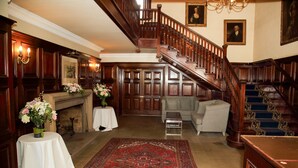 Ein prächtiger Eingangsbereich mit Treppe, Kamin und einem großen roten Teppich.
